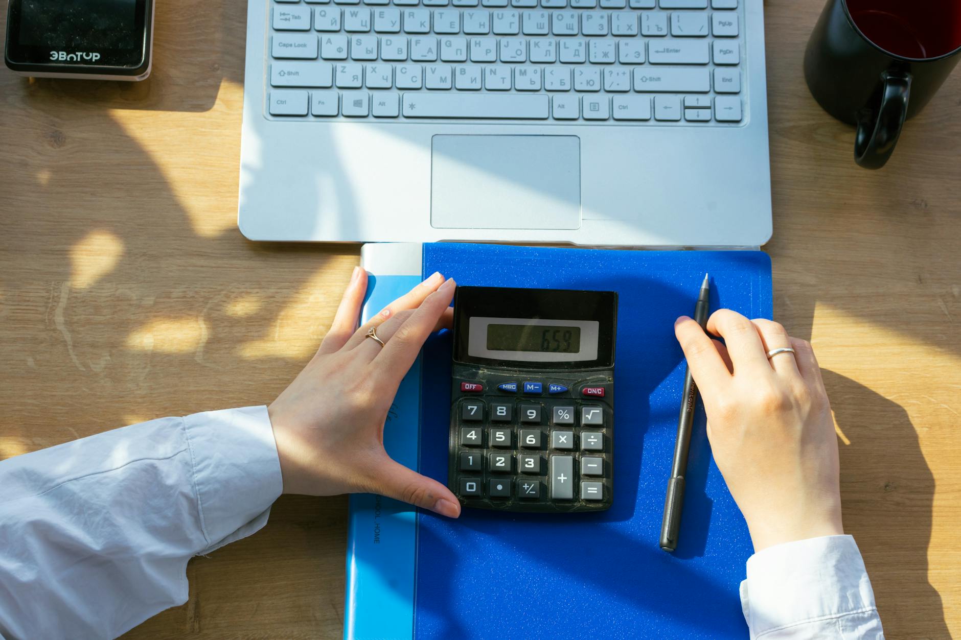 Hands using calculator on a desk with a laptop, pen, and notebook. Perfect for o