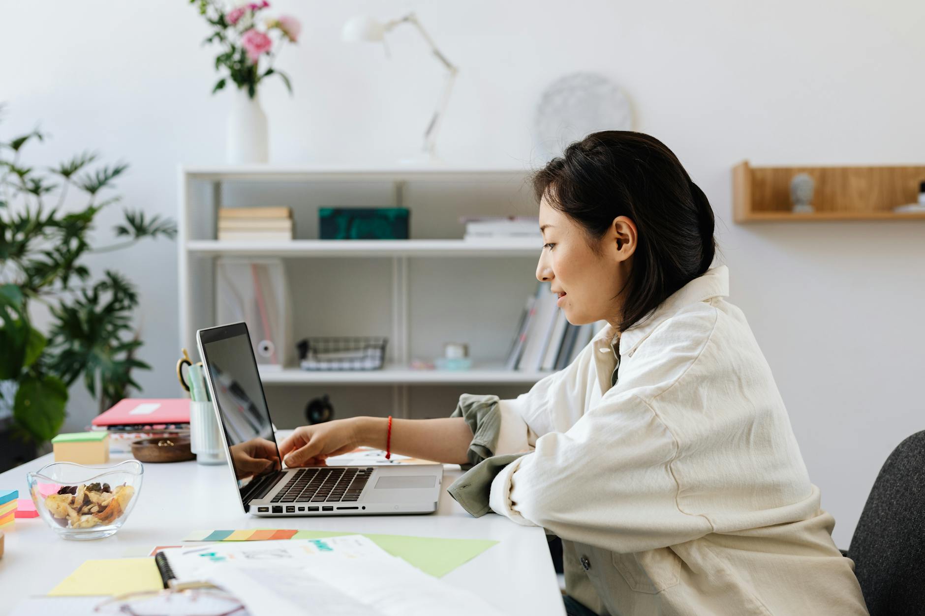 Professional Asian woman working on a laptop in a stylish, plant-decorated offic